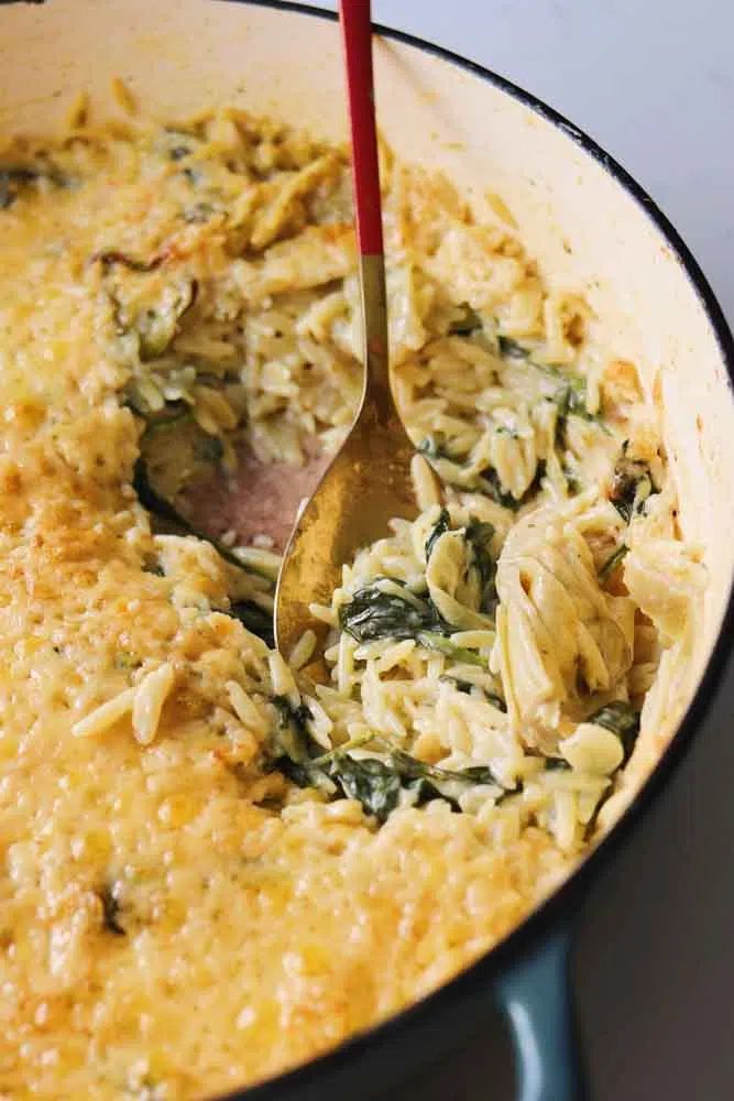 a red spatula is being used to stir food in a pan with spinach and cheese