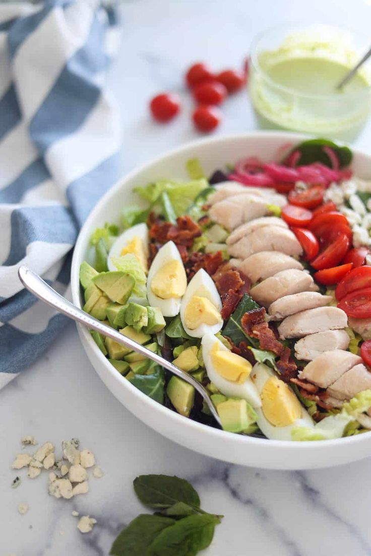 a white bowl filled with meat and veggies on top of a marble counter