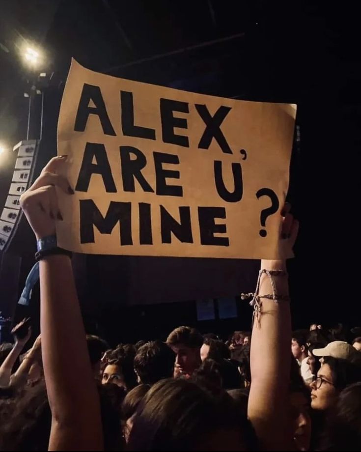 a person holding up a sign that says alex are u mine? at a concert