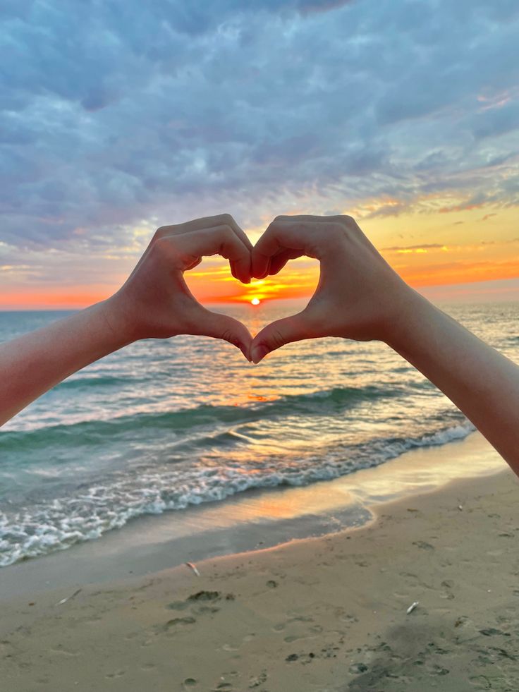 two hands making a heart shape at the beach