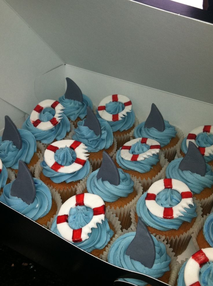 cupcakes decorated with blue frosting and shark fin shapes are in a box