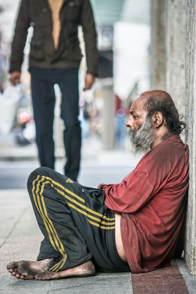 an old man sitting on the ground next to a wall with his feet up and one foot down