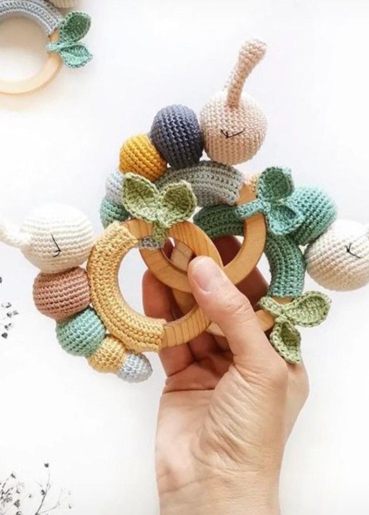 a hand holding a crocheted wooden ring with leaves and flowers on it, surrounded by other crocheted toys