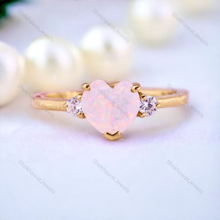 a pink opal heart shaped ring with three diamonds on the side and pearls around it