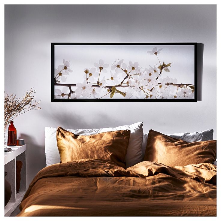 a bed with brown sheets and white flowers on the headboard, framed above it