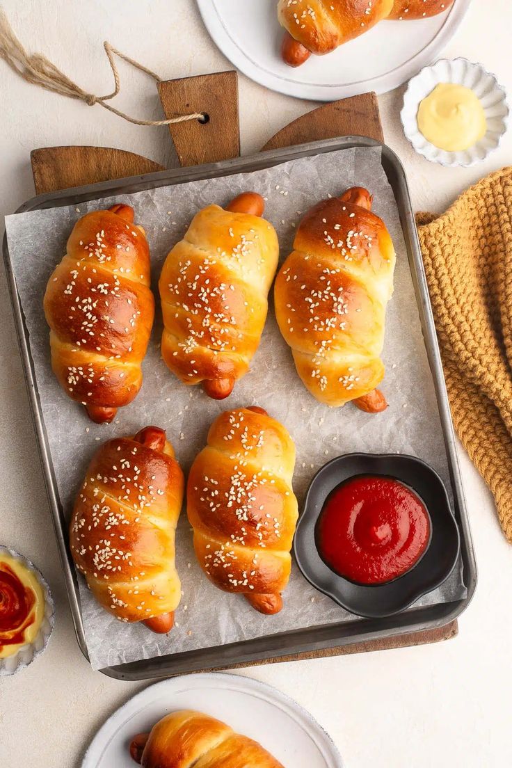 several croissants with sesame seeds and ketchup on a baking sheet