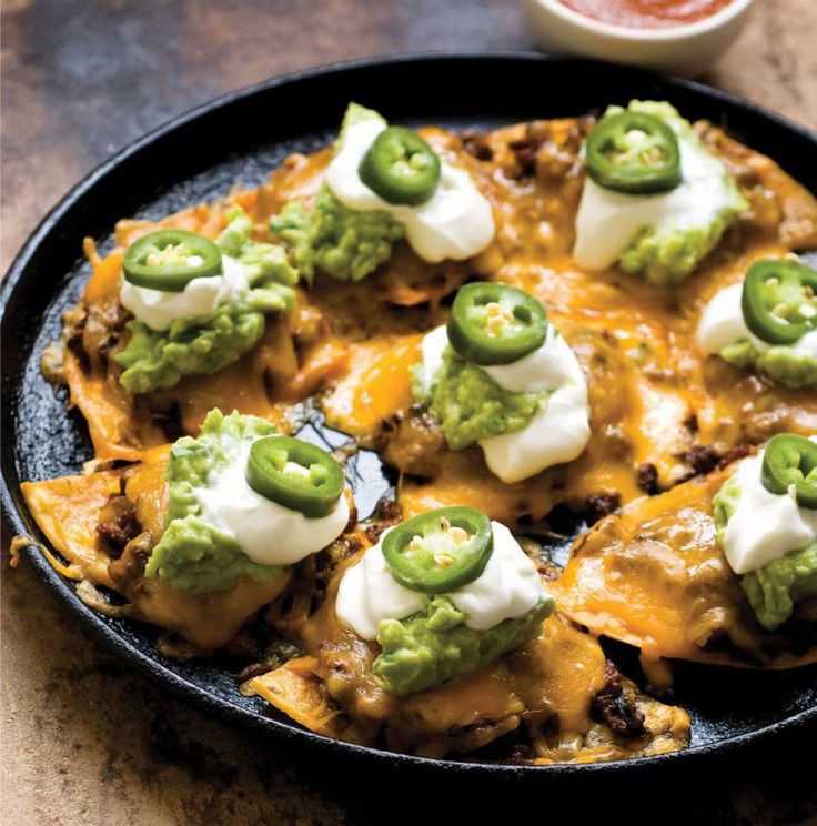 a black plate topped with nachos covered in cheese and guacamole