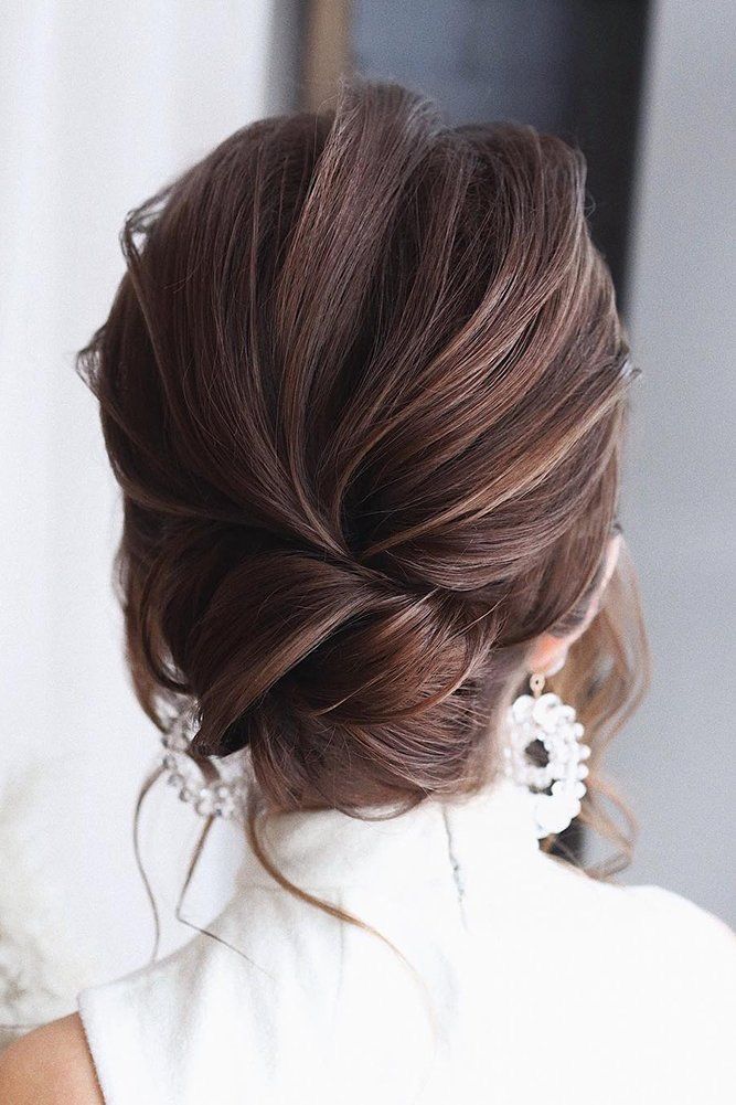 a woman with her hair in a low updo, wearing earrings and a white dress