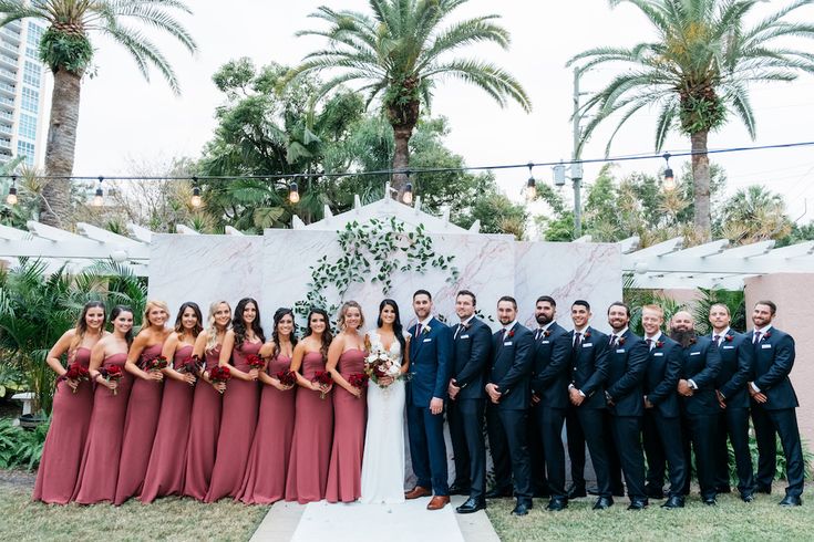 a group of people standing next to each other in front of a wall with palm trees