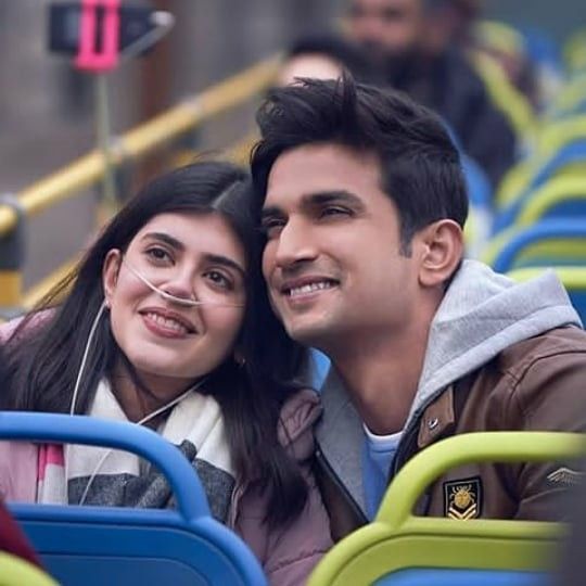 a man and woman sitting next to each other on a bus seat with people in the background