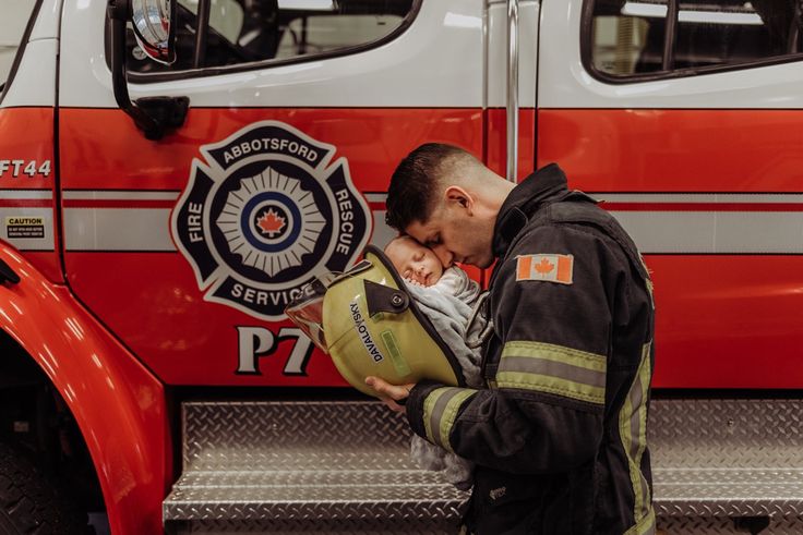 a fireman holding a baby in front of a fire truck