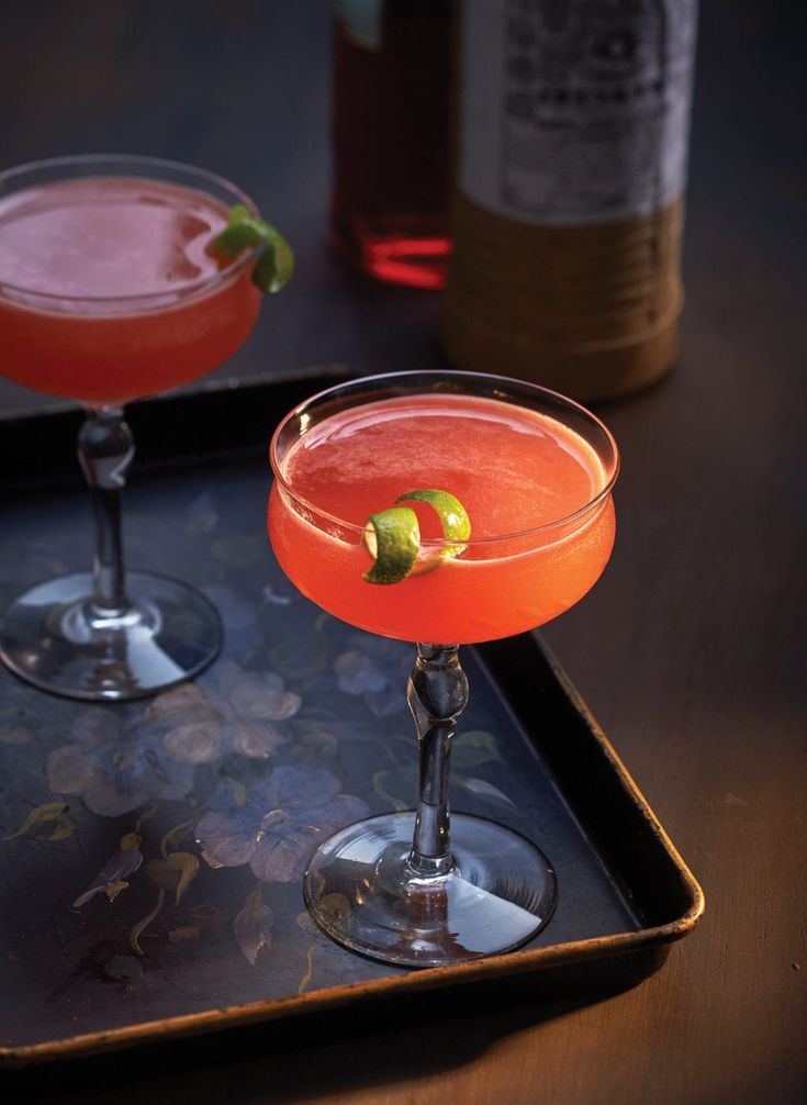 two cocktails sitting on top of a tray next to each other