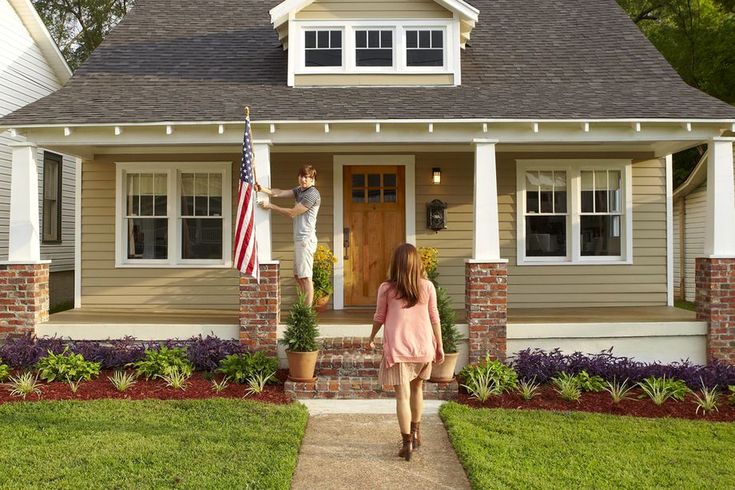 a woman walking towards a house with an american flag on the front door and a man holding a statue