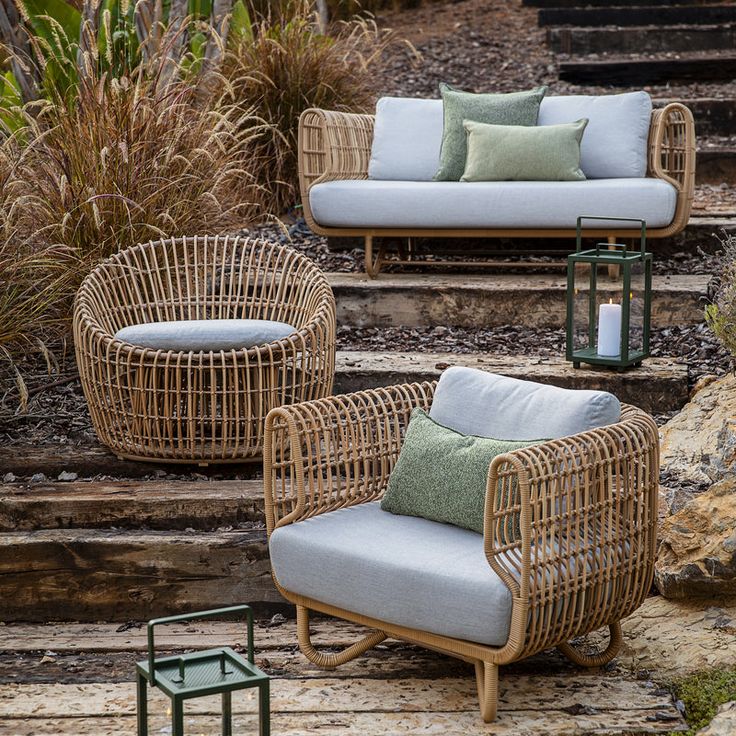 three wicker chairs and two side tables sitting on some steps with plants in the background