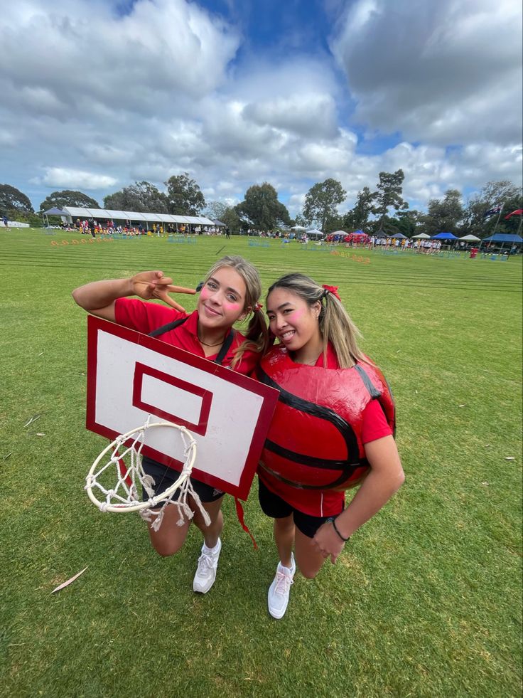 two girls in life vests hold up a basketball hoop on the grass at a park