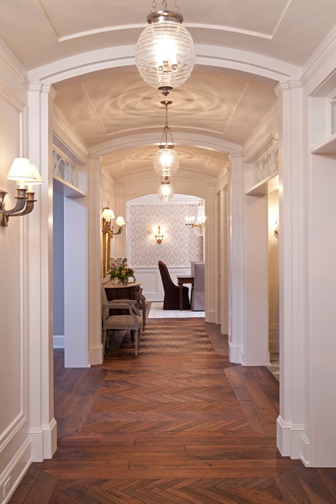 a long hallway with wood flooring and white trim on the walls is lit by two lamps