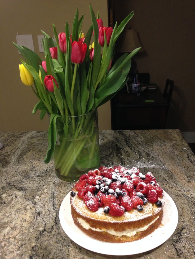 a cake sitting on top of a counter next to a vase filled with tulips