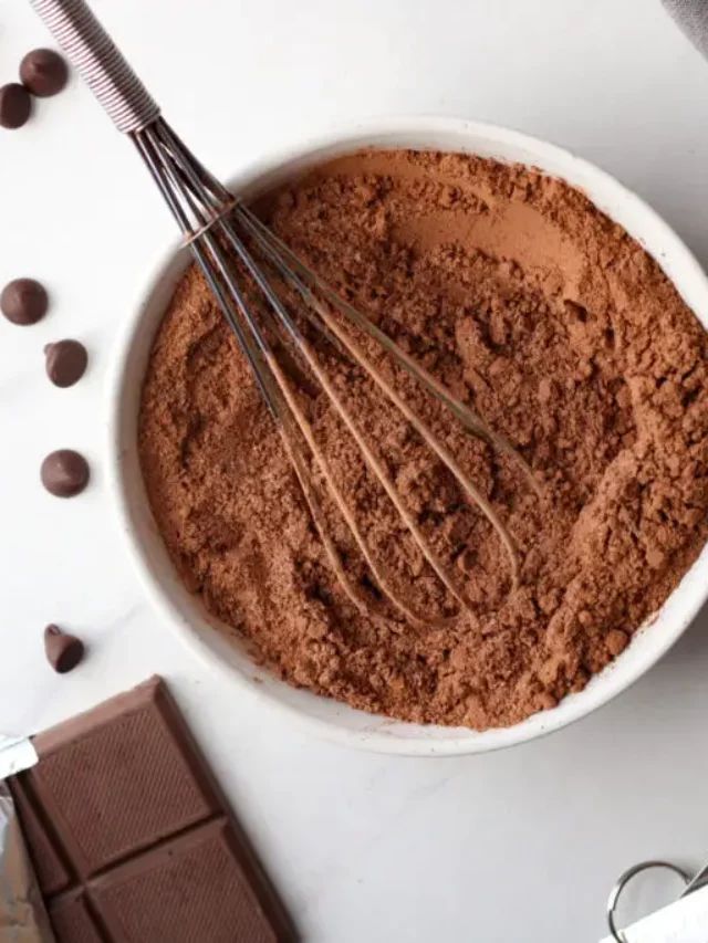 a white bowl filled with chocolate and whisk on top of a table next to some spoons