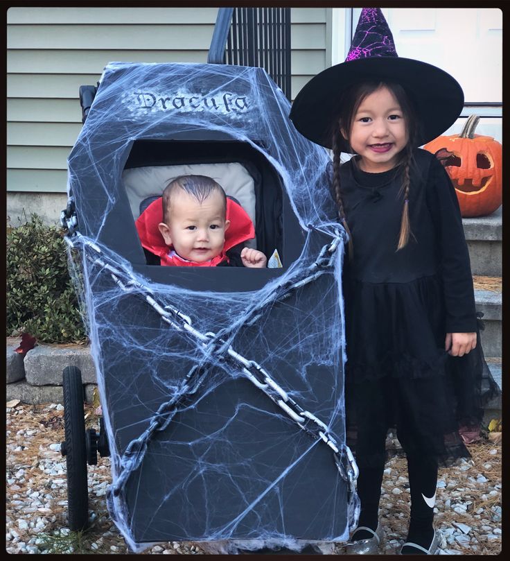 two children dressed up as witches and one is in a stroller with a baby inside