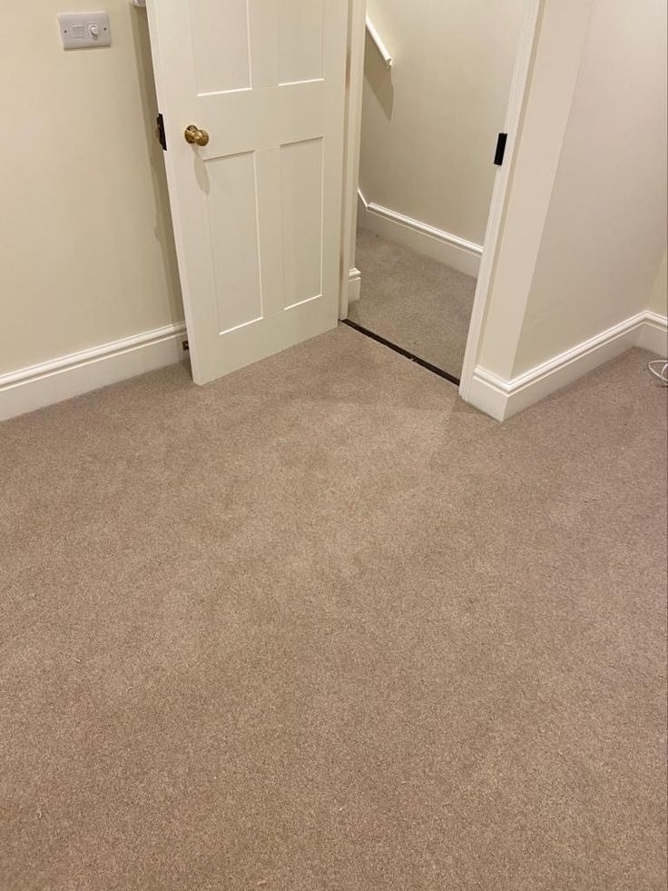 an empty room with a door and carpeted floor in front of the doorway to another room