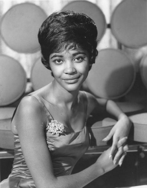 a black and white photo of a woman sitting in front of a wall of speakers