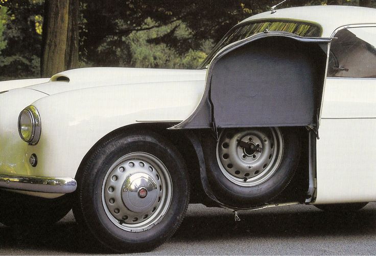 an old white car is parked on the side of the road in front of some trees