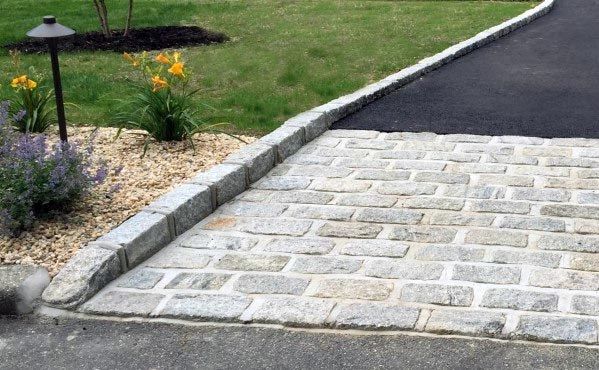 a paved driveway with stone edging and landscaping