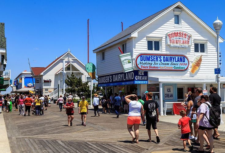 many people are walking on the boardwalk in front of some shops and restaurants at an oceanfront