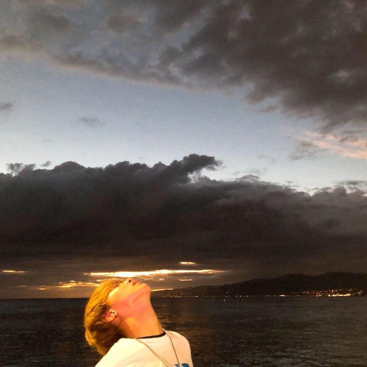 a woman looking up into the sky while standing on a boat in the ocean at sunset