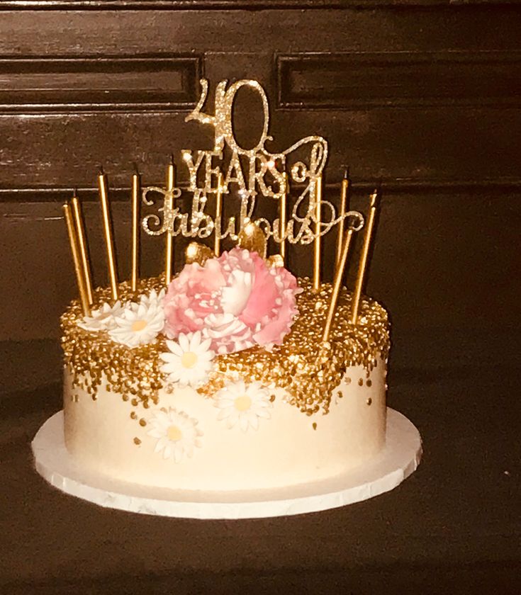 a birthday cake decorated with gold and white frosting, topped with pink carnations