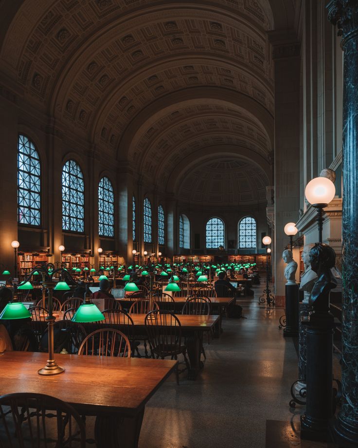 a large room filled with lots of wooden tables and green lamps on top of them