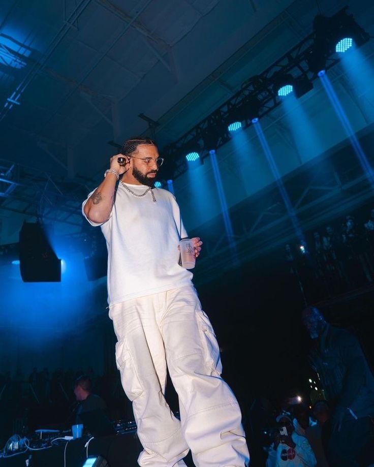 a man standing on stage with his cell phone to his ear and wearing white pants