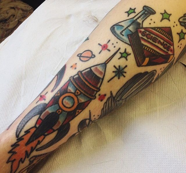 a tattoo on the arm of a person with a rocket ship and stars around it