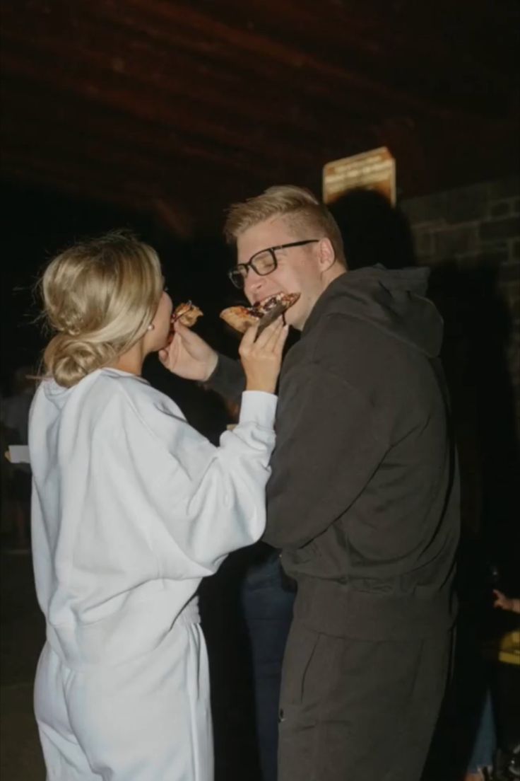 a man and woman standing next to each other while eating food from their mouths in front of them