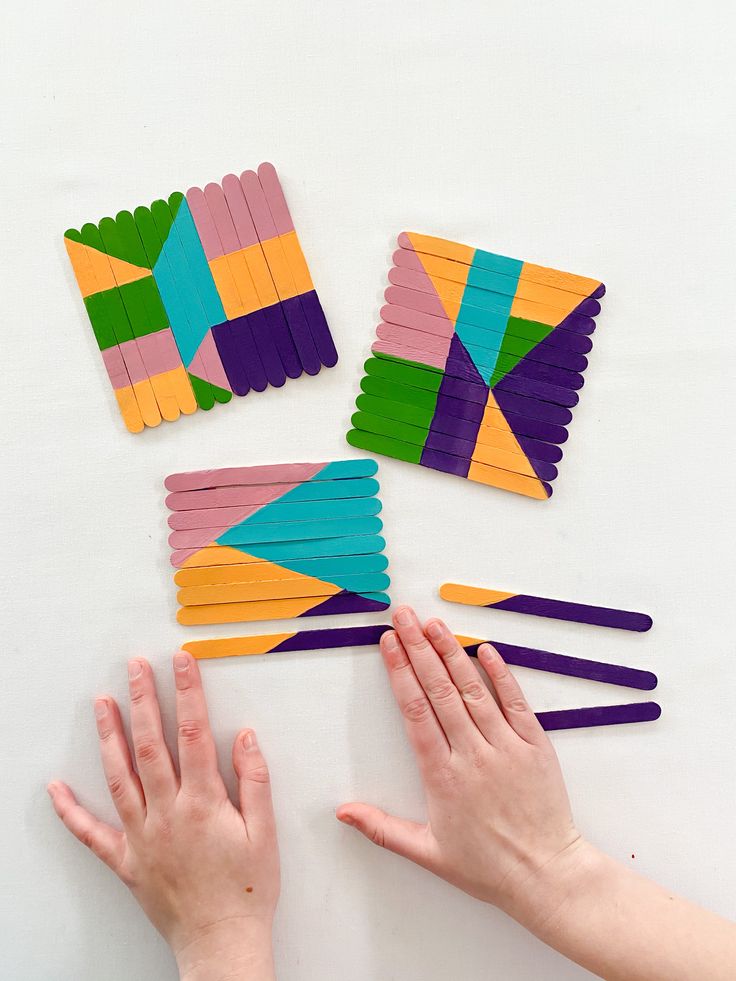 several pieces of colored paper are arranged on a table with two hands reaching for them