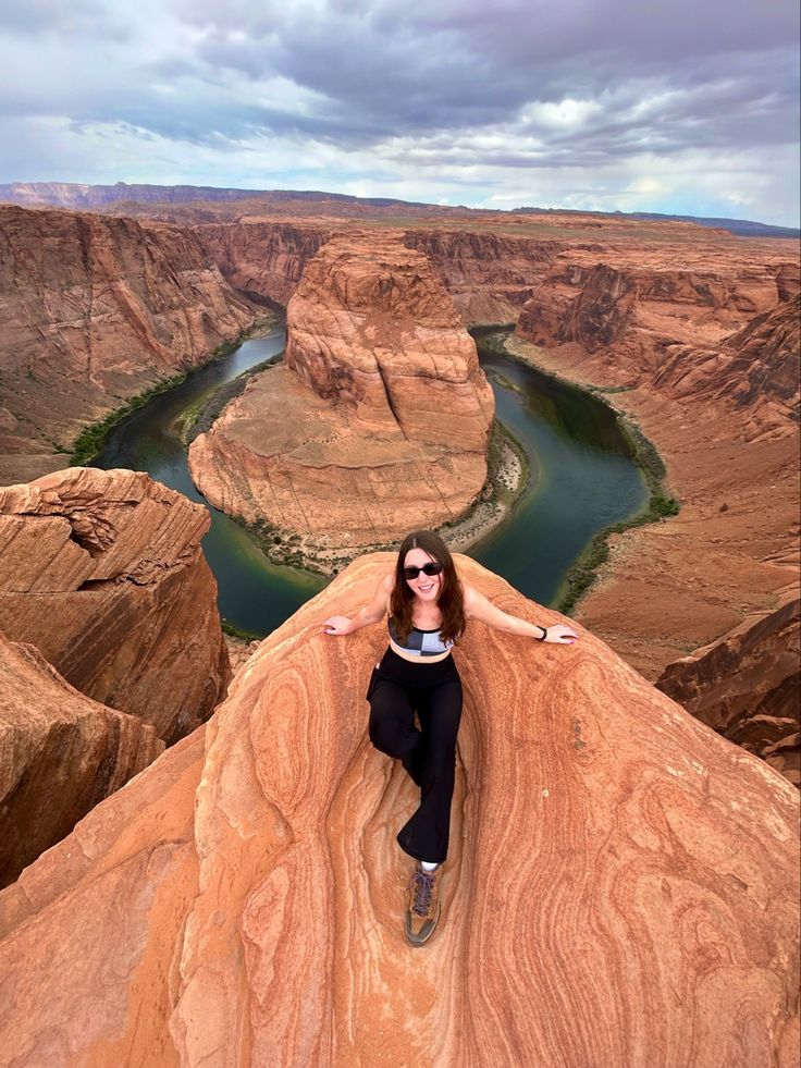 a woman sitting on top of a cliff next to a river