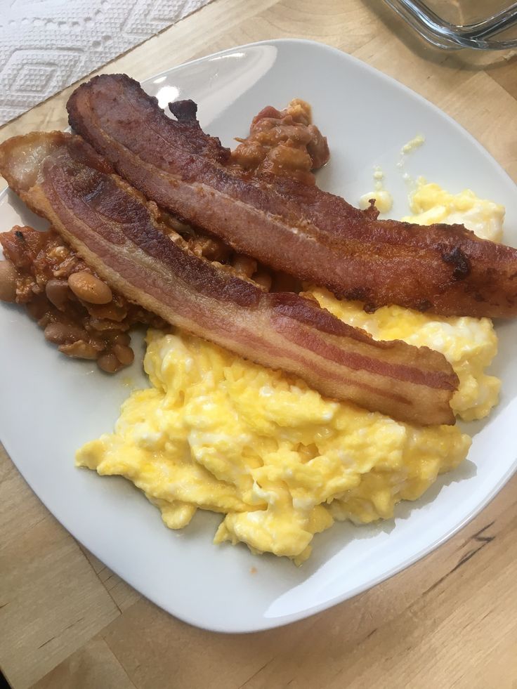 a white plate topped with eggs, bacon and hash browns on top of a wooden table