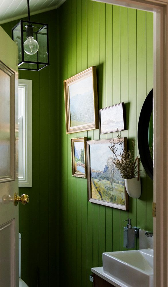 a bathroom with green walls and pictures hanging on the wall above the sink, along with a white toilet