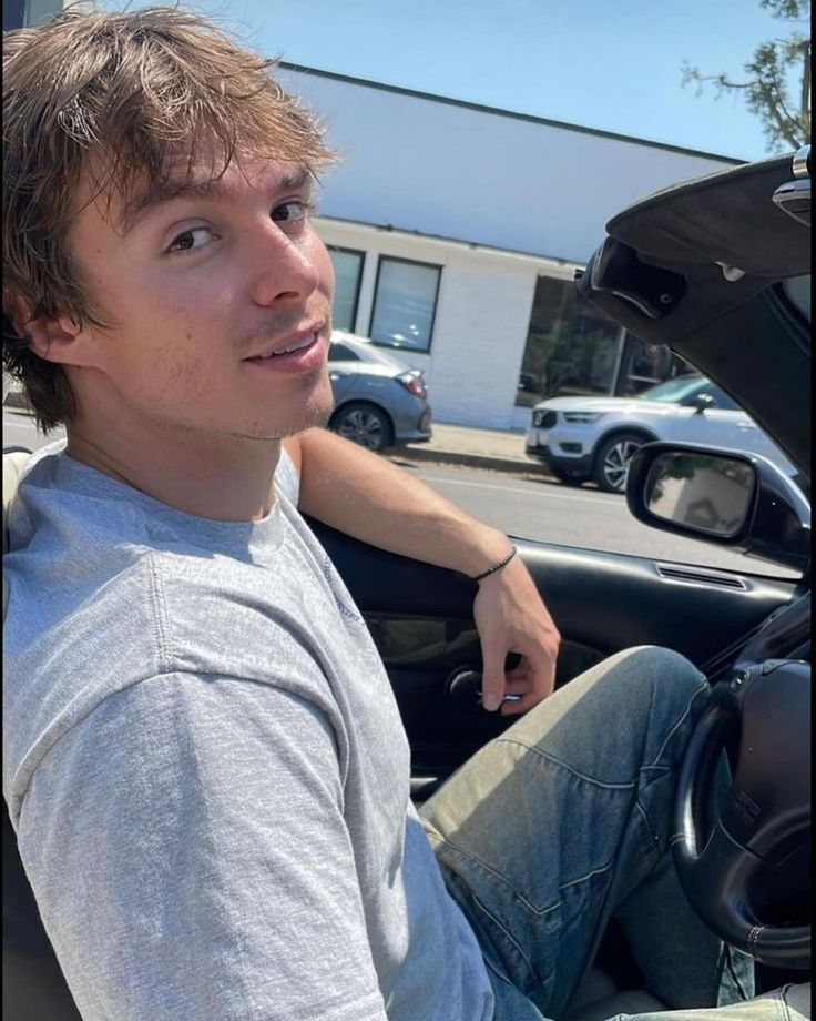 a young man sitting in the driver's seat of a car with his hand on the steering wheel