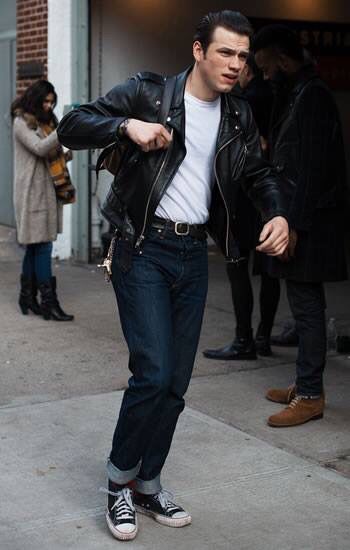 a man in black jacket and white t - shirt standing on sidewalk next to people