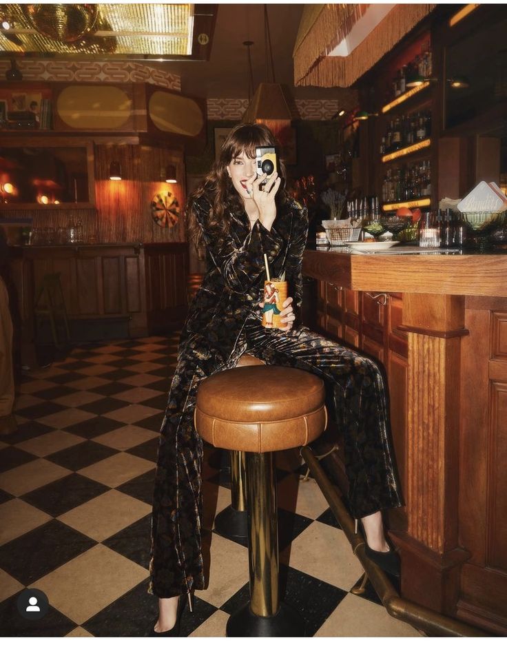 a woman sitting on top of a stool next to a bar with a camera in her hand