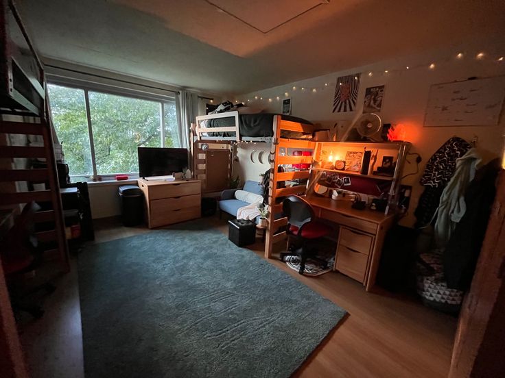 a dorm room with bunk beds, desks and other items on the floor in front of a large window