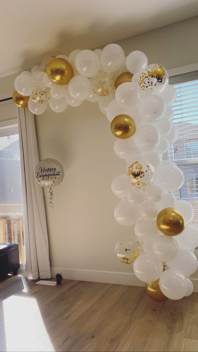 a balloon arch with gold and white balloons hanging from it's sides in front of a window