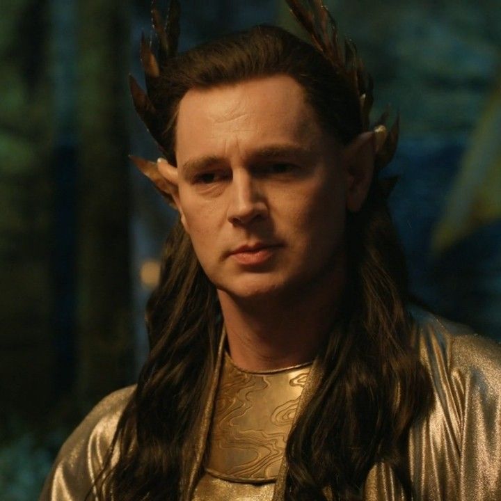 a man with long hair and horns on his head wearing gold clothes in the woods