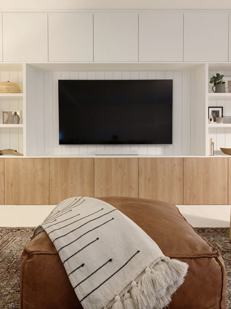 a large flat screen tv mounted on the wall above a leather ottoman in a living room