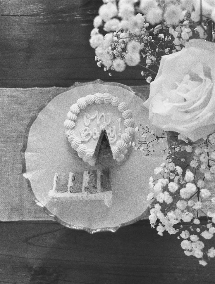 an old photo of a cake on a plate next to flowers and a vase with roses