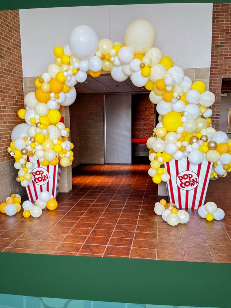 an arch made out of balloons and popcorn buckets is decorated with yellow and white balloons