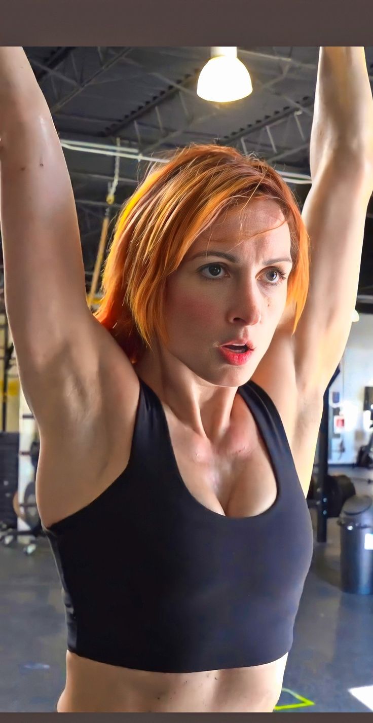 a woman with red hair is flexing her arms and shoulders in a crossfit gym