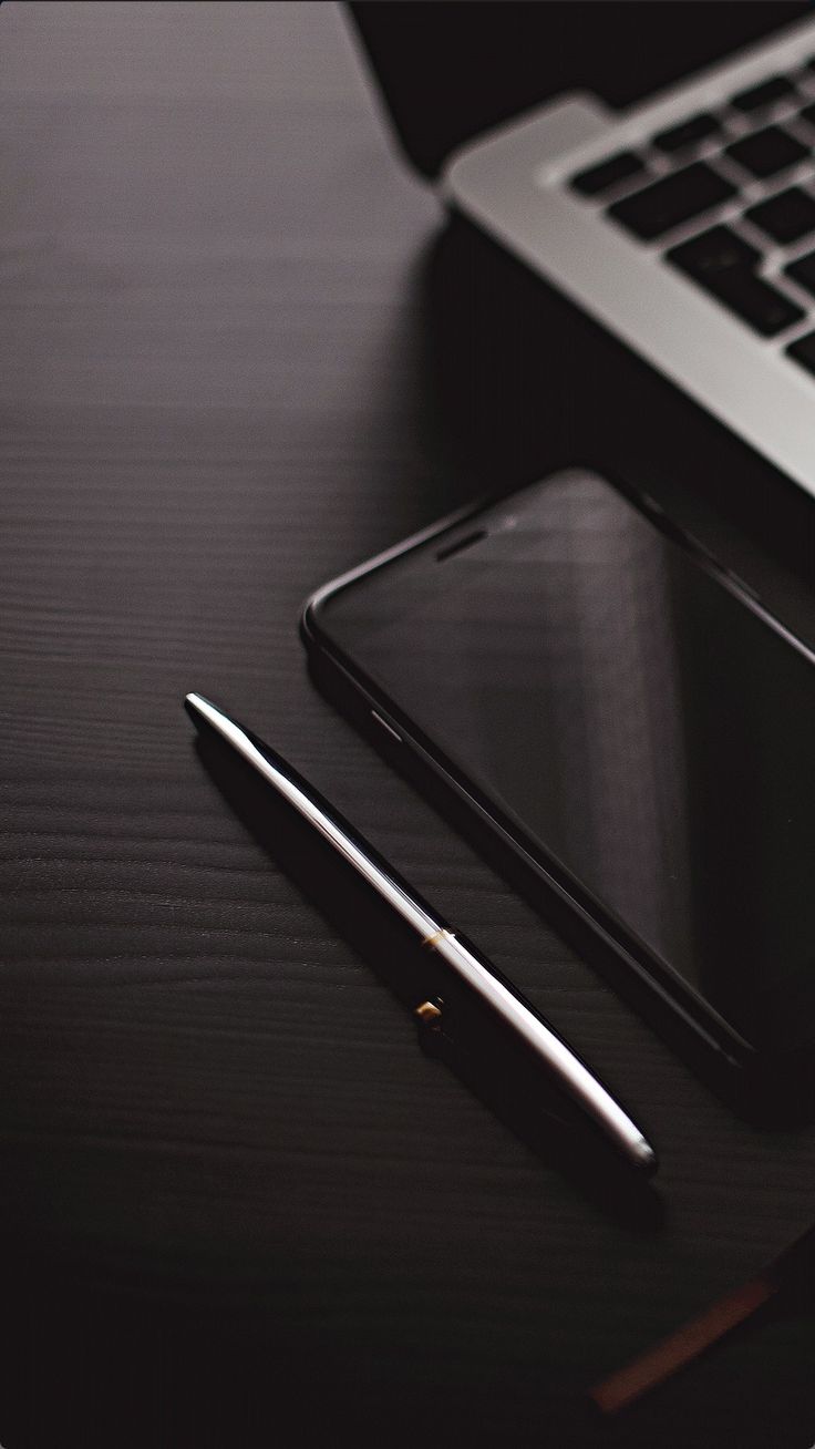 a cell phone, pen and laptop on a desk