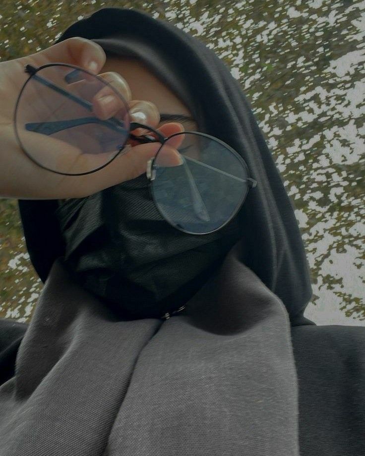 a person wearing a black hood and holding some glasses in front of their face with trees in the background